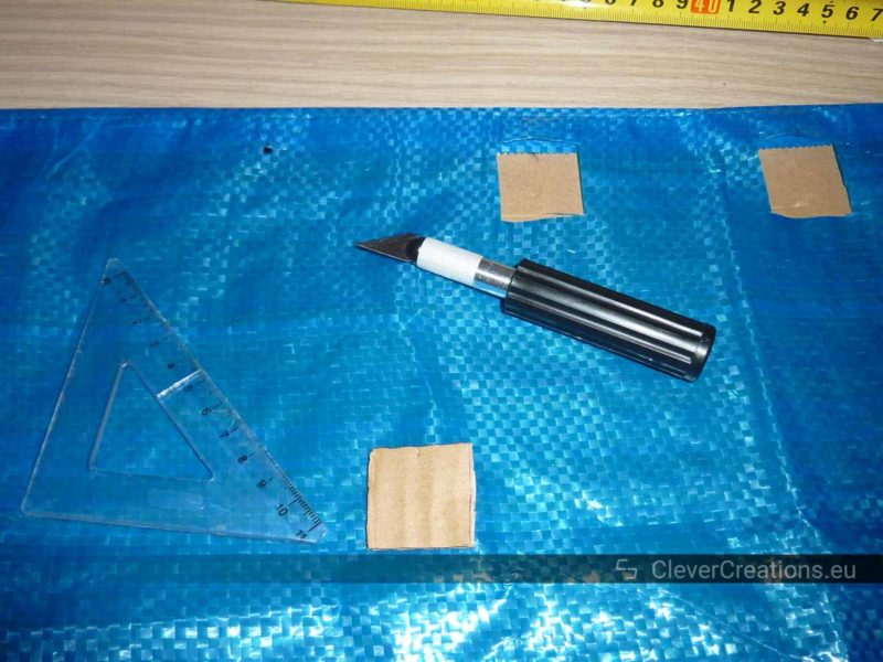 An IKEA FRAKTA bag with several square holes cut out of it, with on top a drafting triangle, cutting template and a sharp blade.