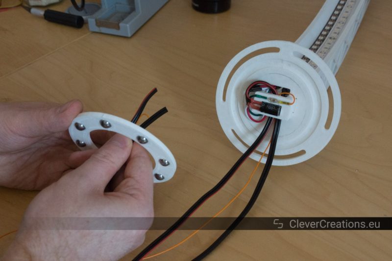 A hand inserting wires through a white 3D printed thrust bearing with in the background a white 3D printed desk lamp.