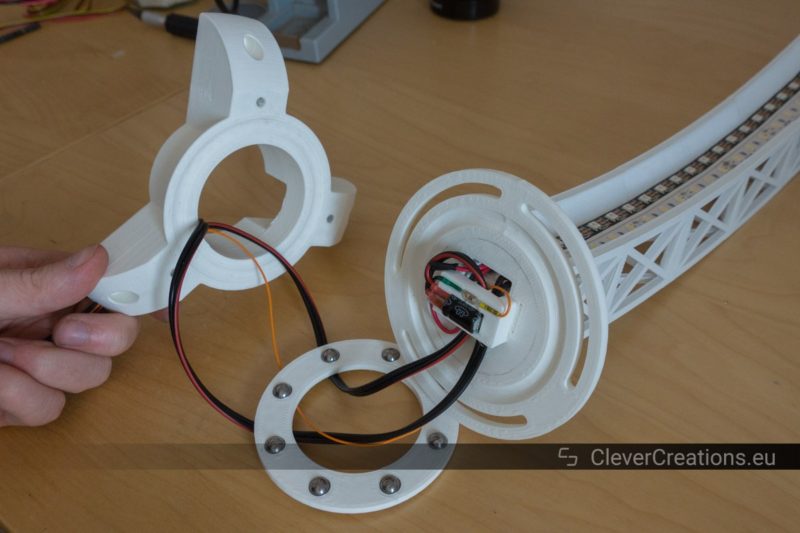 A hand holding a white component up so that the path that wires take through a 3D printed thrust bearing is clearly visible.