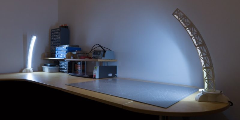 Two custom 3D printed rotating desk lamps on top of a desk with tools and containers.