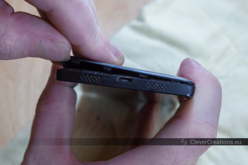 Two hands holding a LG Nexus 5 phone and removing the back cover.