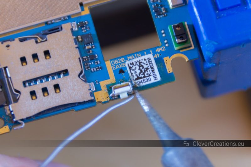 A solder iron with solder being used to solder a power button on a phone motherboard.