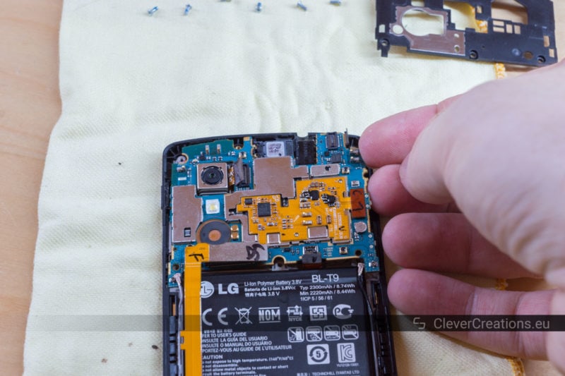 A hand carefully lifting the motherboard out of a LG Nexus 5 phone.