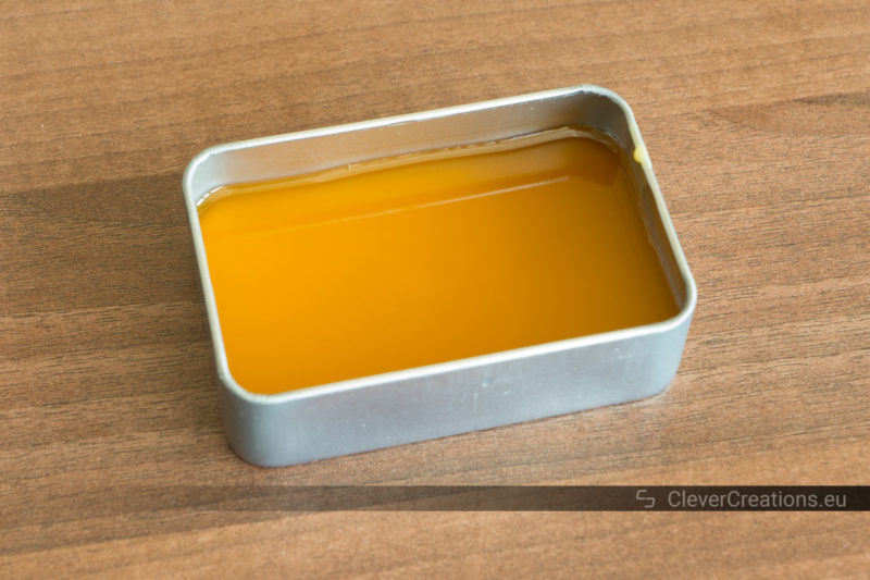 Liquid shoe wax in a tin storage container without lid that is placed on a wooden surface.
