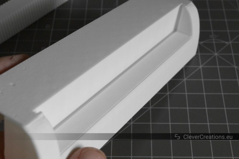 A white 3D printed handle with in the background support material that has been removed.