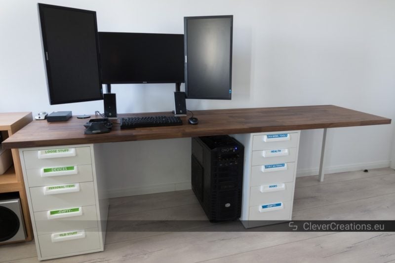 Front view of a desk composed out of an IKEA KARLBY walnut countertop and two white IKEA ALEX drawer units with 3D printed handles and blue and green labels.