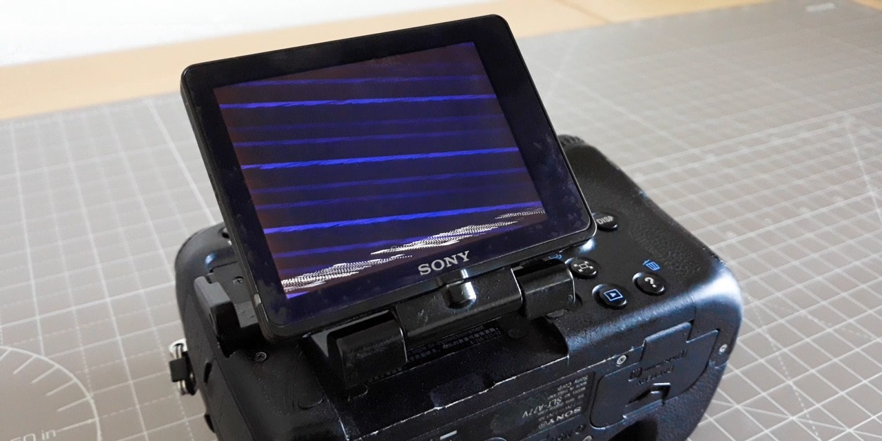 A Sony A77 camera with a broken LCD screen displaying artifacts.