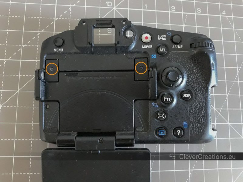 A detached rear cover of a Sony SLT-A77 camera. Two exposed screws that are located under the LCD are circled.
