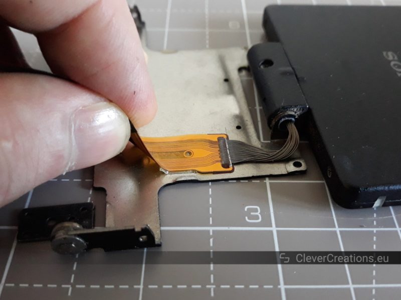 A hand peeling off a flex cable from a metal plate in a LCD assembly.