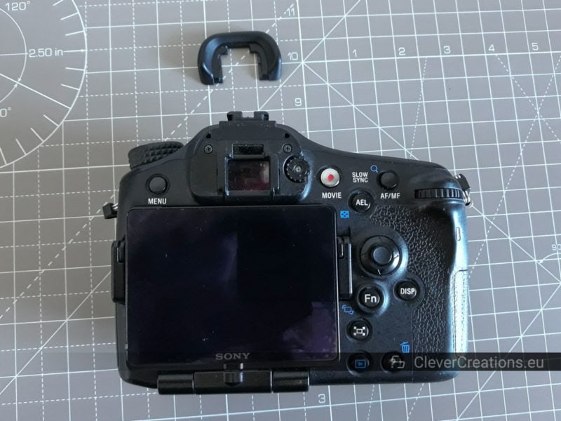 A Sony SLT-A77 camera body with placed above it its detached rubber eye cup.