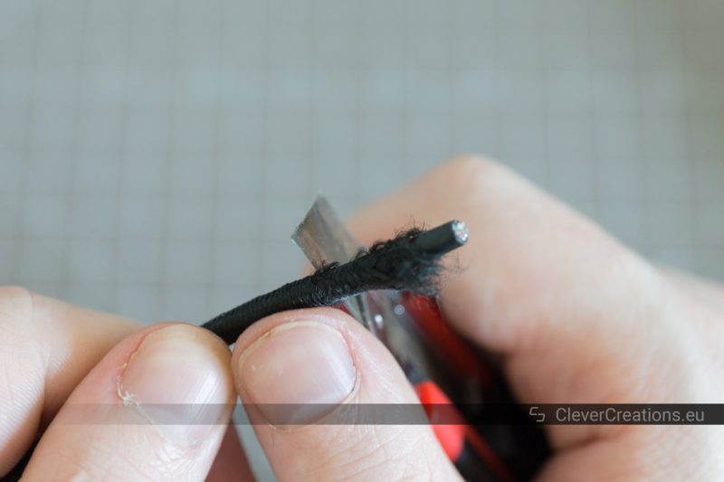 A hand using a box knife to remove the braided sleeving of a USB cable.