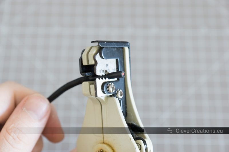 A wire stripper tool being used to remove the insulation from a USB cable without connector.