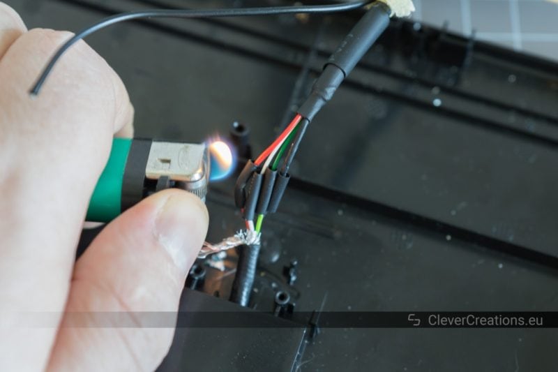 A hand holding a lighter that is being used to shrink four small pieces of heat shrink tubing on the wires of a USB cable.
