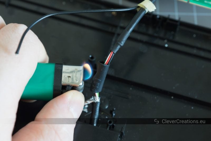 A hand holding a lighter that is being used to shrink a large piece heat shrink on the wires of a USB cable.