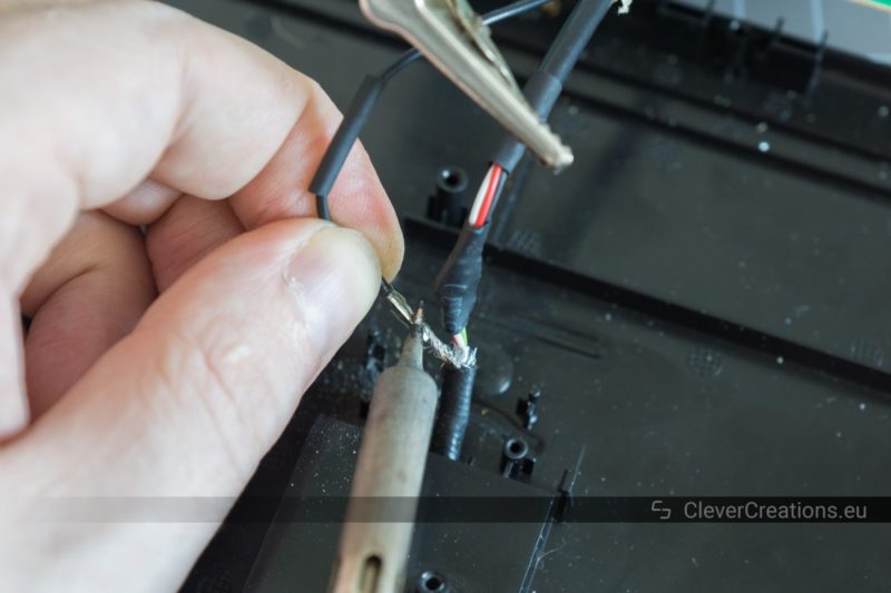 A hand holding a piece of wire that is simultaneously being soldered to a second piece of wire using a soldering iron.