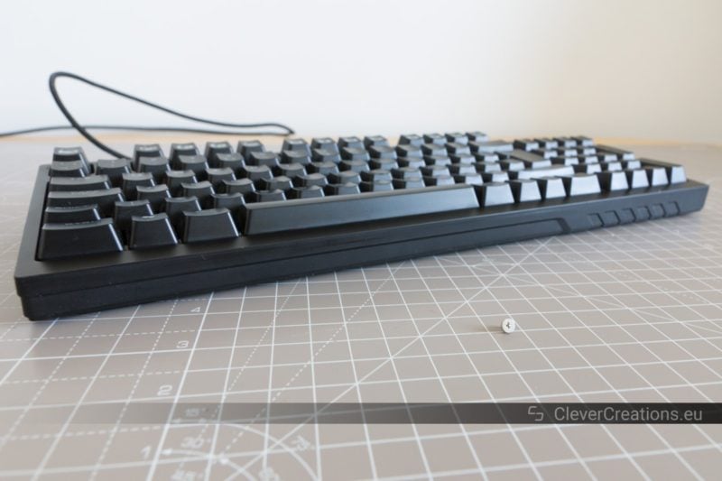 A Cooler Master Quickfire TK keyboard with in front of it a tiny screw.