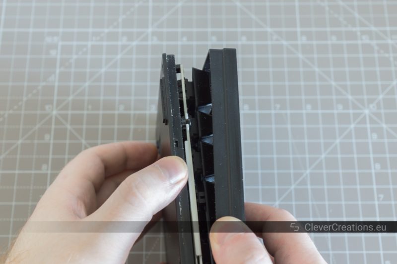 Two hands separating the unscrewed top and bottom halves of a Cooler Master Quickfire keyboard.