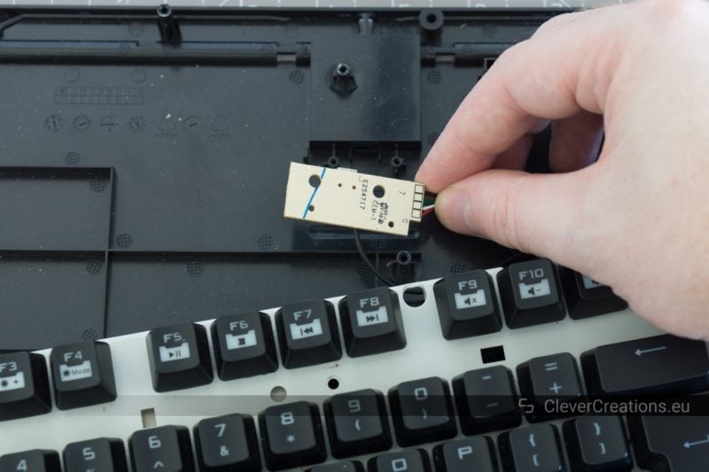 A hand holding a small PCB of a computer keyboard, with in the background the disassembled keyboard.