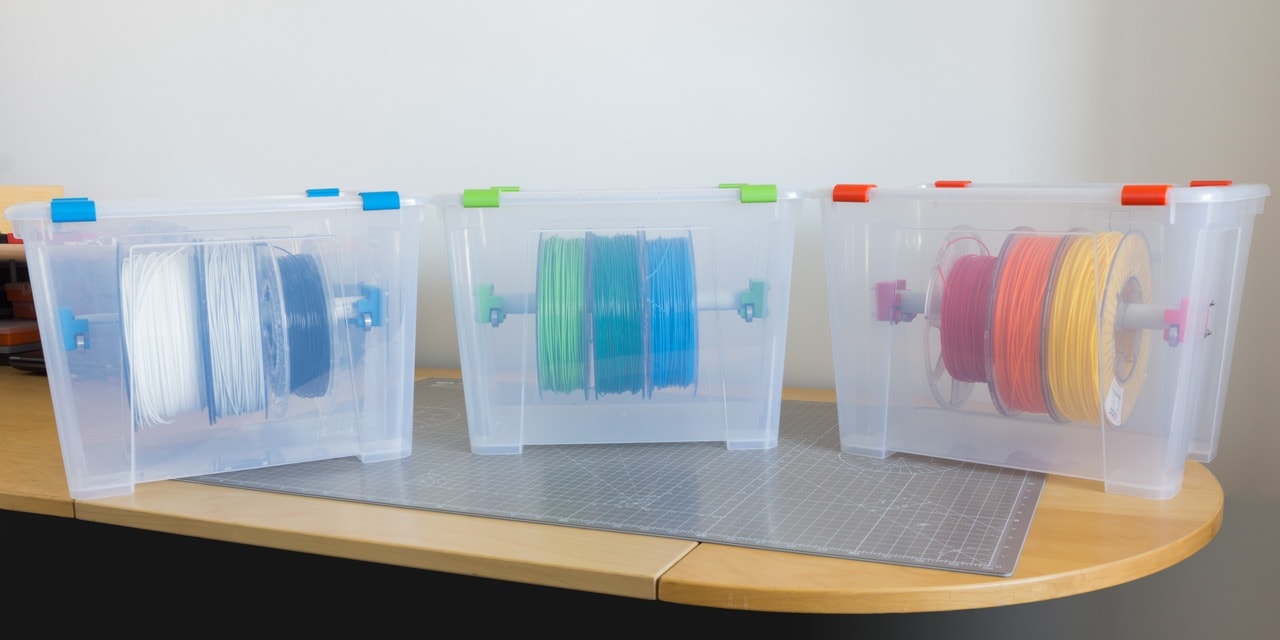 Three 3D printer filament storage boxes containing various rolls of colorful 3D printer filament.