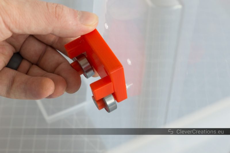 A hand inserting red 3D printed components for a filament storage system into an IKEA SAMLA box.