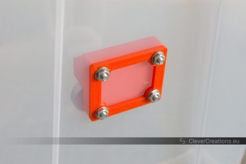 A red plastic assembly that is attached to an IKEA SAMLA box with M4 bolts and nuts.