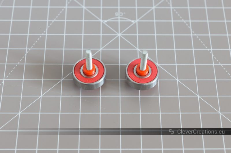 Two M4 bolts with a 608-RS2 bearing and a red 3D printed bearing retainer slid over each bolt.
