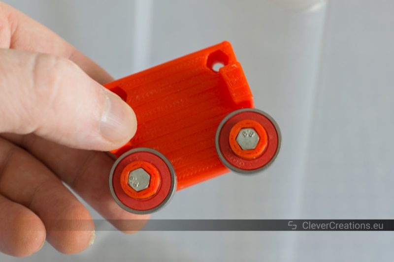 A hand holding a 3D printed base plate for a filament storage system, with two 608-RS2 bearings attached using M4 bolts.
