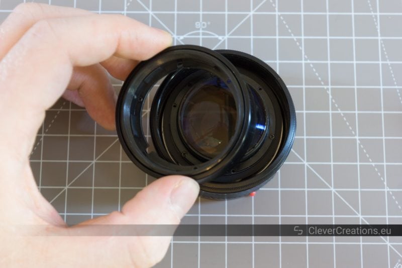 A hand lifting a built-in lens hood out of a partially disassembled camera lens.