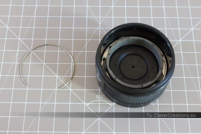 An iris diaphragm retainer spring next to a partially disassembled 50mm prime camera lens.
