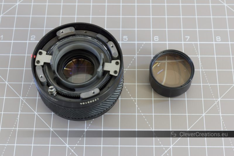 A partially disassembled 50mm prime camera lens with next to its rear ball lens block.