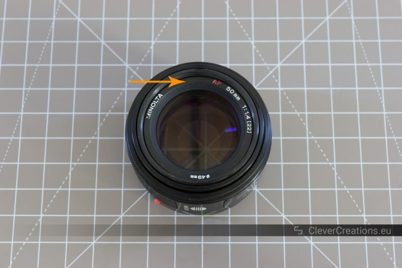 The front of a Minolta 50mm F/1.4 with an arrow pointing to the front decoration ring.