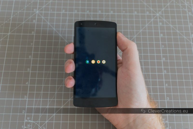 A hand holding an LG Nexus 5 phone which is powering up.