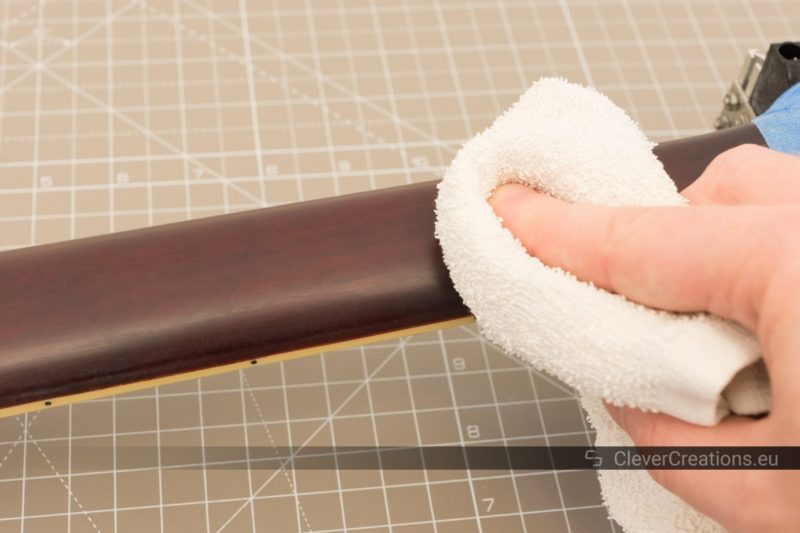 A hand using a cloth to wipe away polyurethane lacquer sanding residue from a sanded guitar neck.