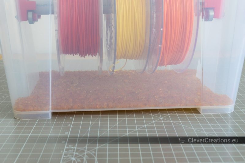 An IKEA SAMLA filament storage box with a layer of reusable silica gel beads to keep the filament dry.