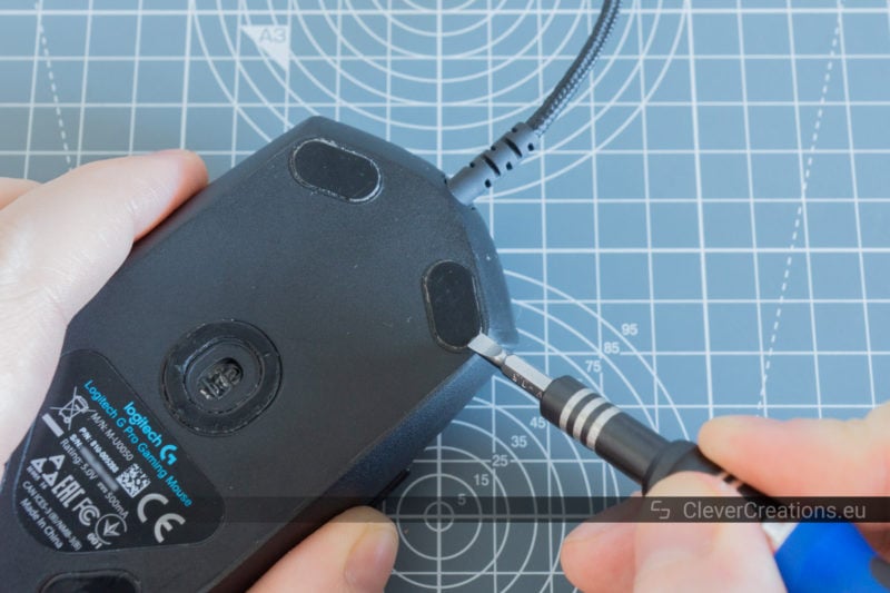 A screwdriver being used to remove the feet on the bottom of a Logitech G Pro mouse.