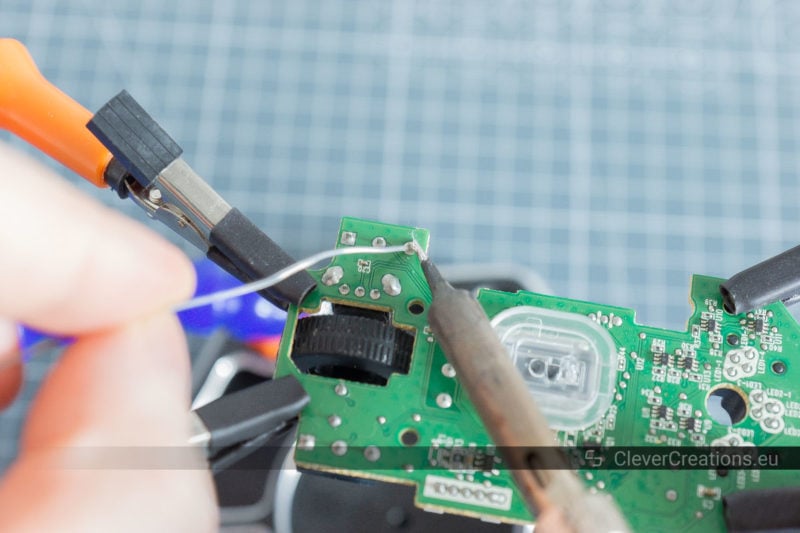 A hand adding solder to the solder joint of a microswitch on the underside of a circuit board.