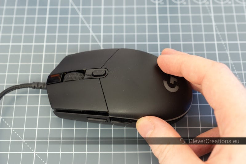 A hand placing the top plastic cover of a mouse casing on top of the bottom half of the casing.