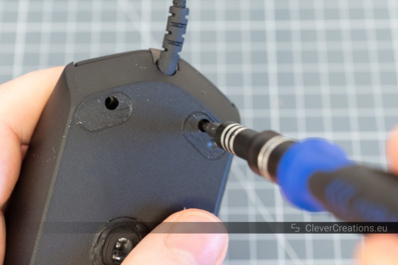A screwdriver screwing in the screws on the underside of a gaming mouse.