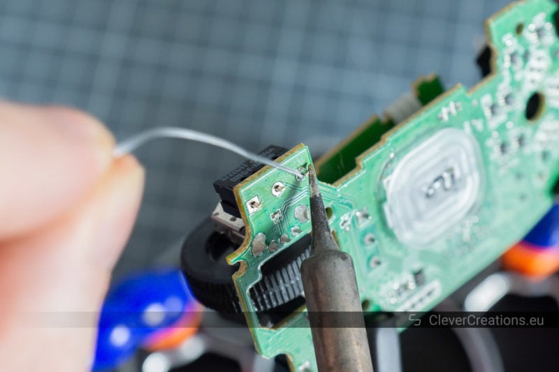 A soldering iron and solder being used to solder a pin of a D2FC-F-7N microswitch to a PCB.