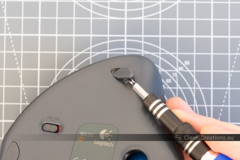 A screwdriver removing one of the feet of a trackball mouse.