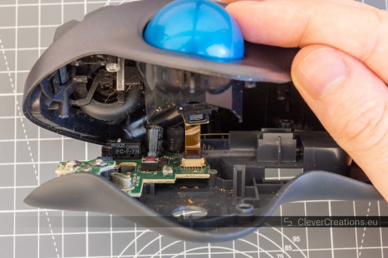 A view of the circuit board and cables of a Logitech M570 trackball that is being held open.