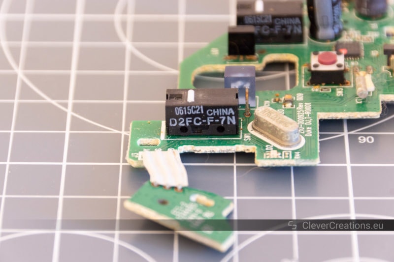 A close-up of a D2FC-F-7N microswitch on a PCB on a desk cutting mat.