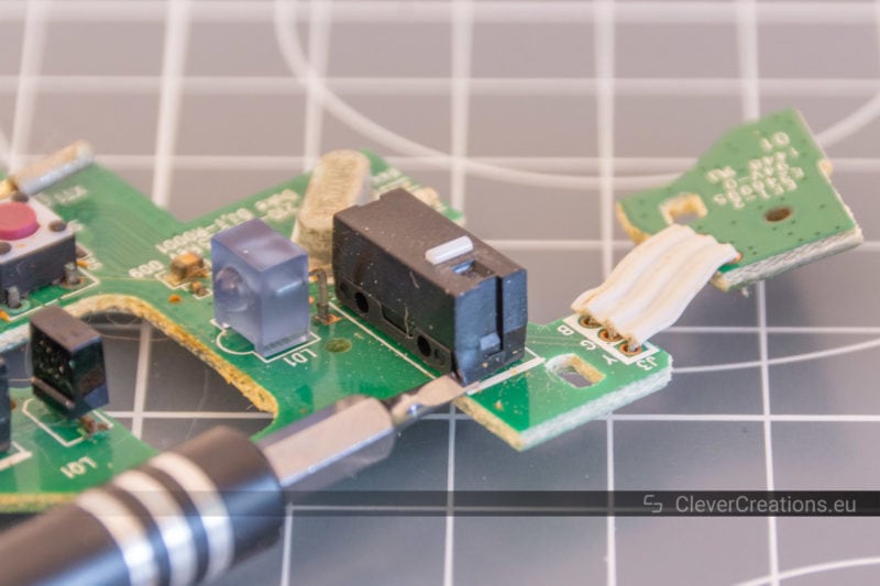 A tiny flathead screwdriver being used to remove the lid of a mouse microswitch.
