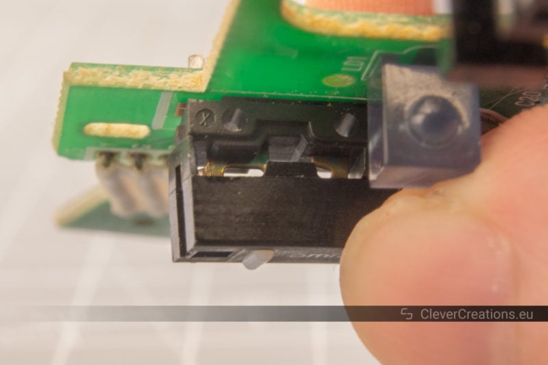 The cover of a microswitch being put back on by a hand while the circuitboard and switch are being held upside down.