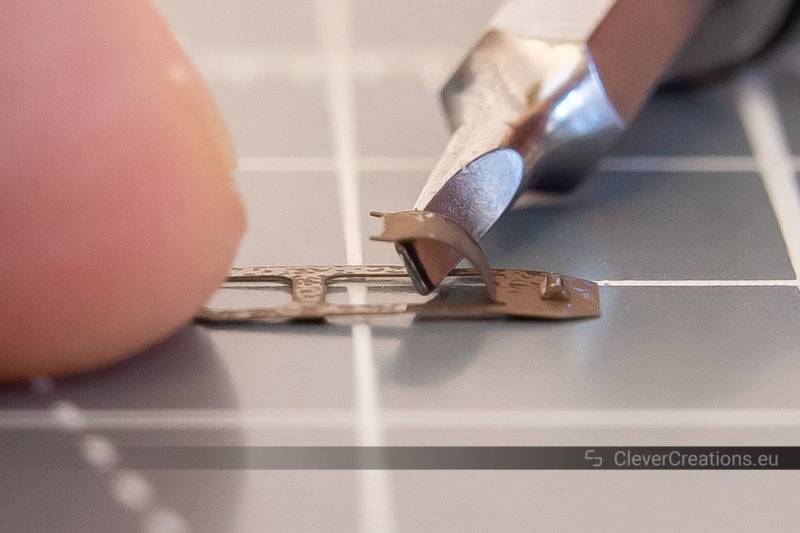 A small flathead screwdriver bending a metal tab on a corroded copper spring mechanism.