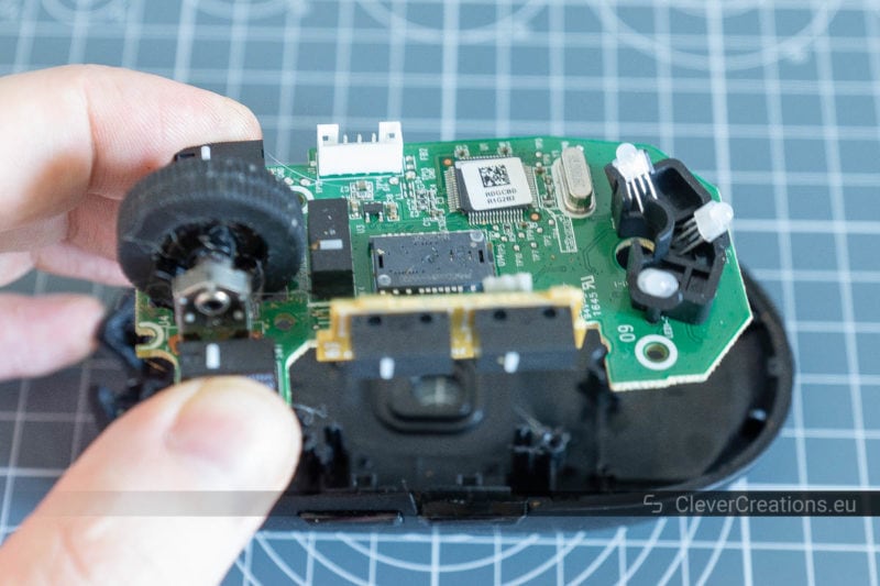 A hand removing the PCB from the plastic casing of a mouse.