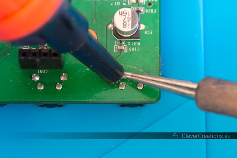 A solder sucker being used to desolder a through-hole component solder joint.