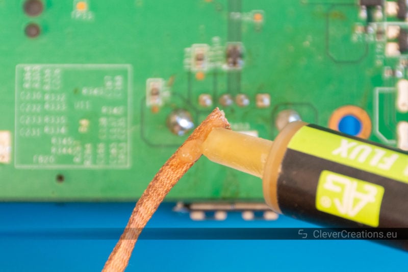 No-clean flux being applied to a piece of soldering wick with in the background a PCB.