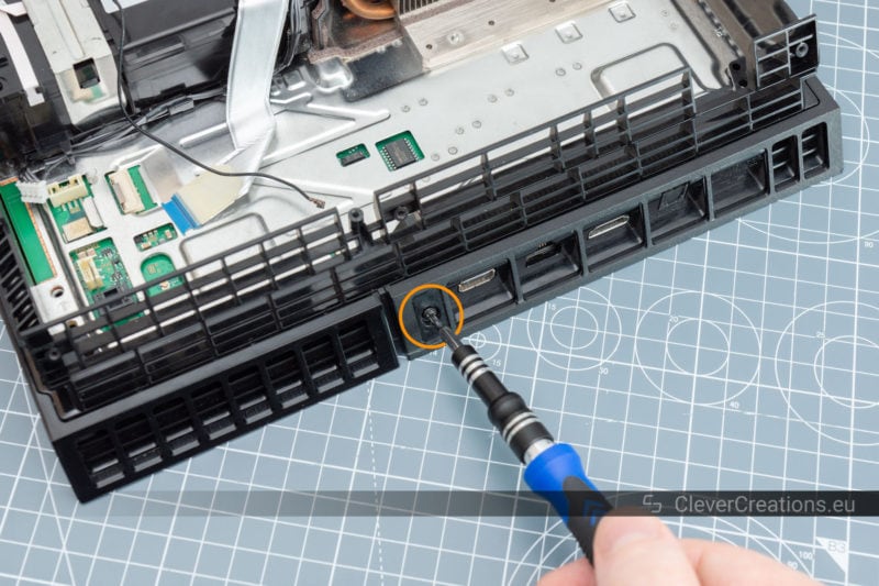 A screwdriver removing a screw from the rear of a PS4 console.