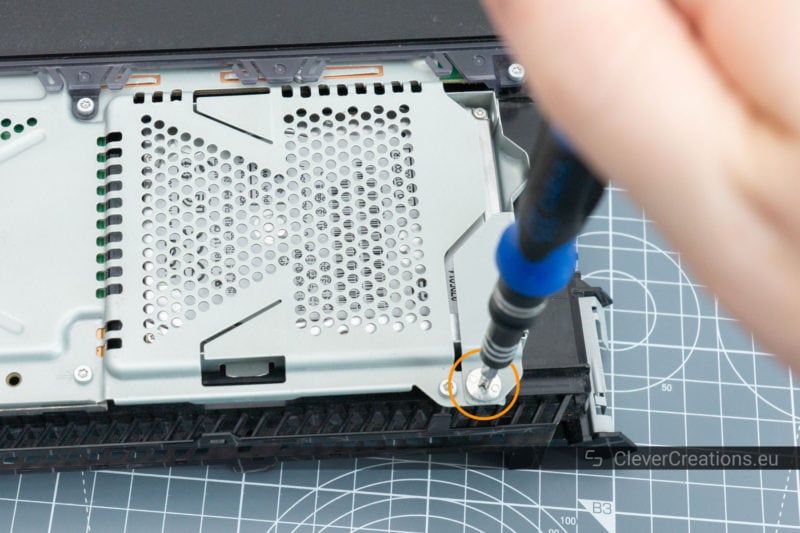 A screwdriver unscrewing the screw that holds the HDD mount of a PS4 in place.